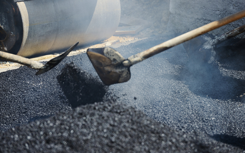 Workers leveling steaming hot mix asphalt for roadwork.
