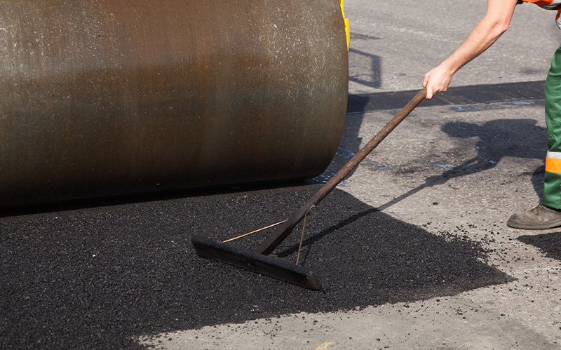A construction worker using a rake to manually level fresh asphalt