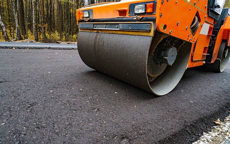 A heavy-duty road roller compacting a fresh layer of hot-mix asphalt on a new road surface.
