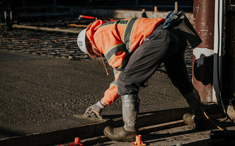Construction worker performing manual road surface repair and maintenance.